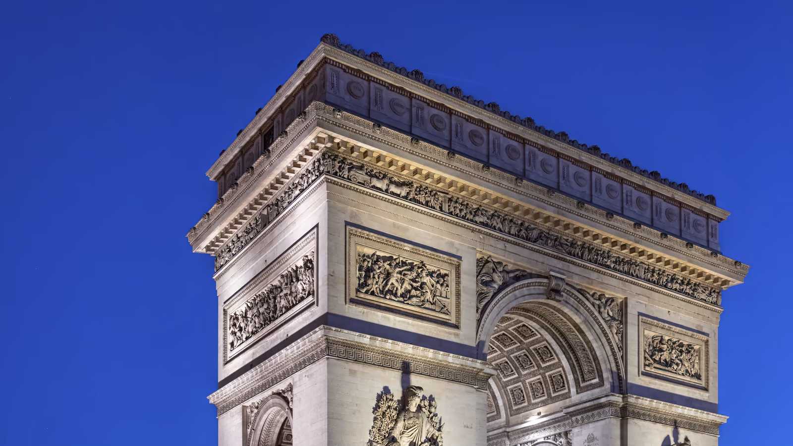 Détail de la façade de l’Arc de Triomphe de l’Étoile sur un ciel bleu, à Paris.